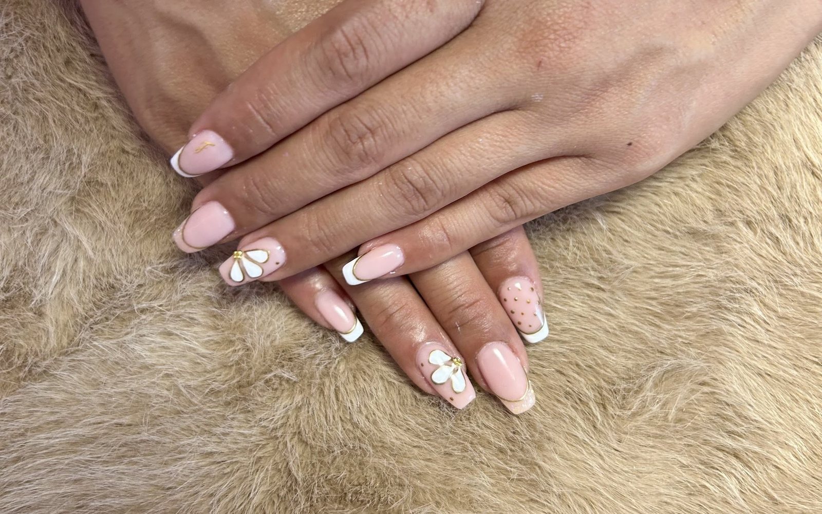 Nude-roze nagels met witte French-randjes en witte 3D-bloemetjes, handen op een beige vacht