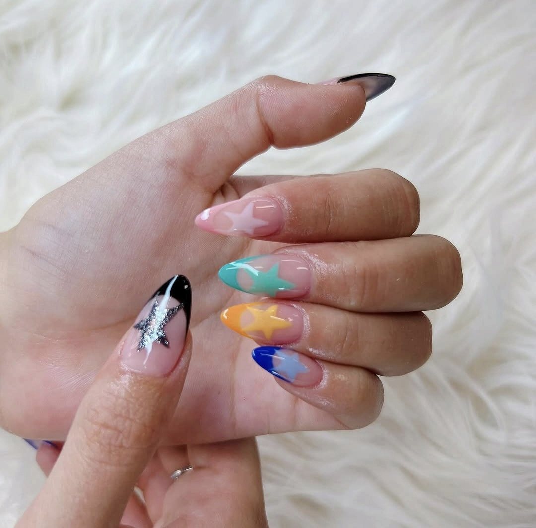 Amandelvormige nagels met pastel sterretjes in roze, mint, oranje en blauw en één zwarte tip met een glitterster