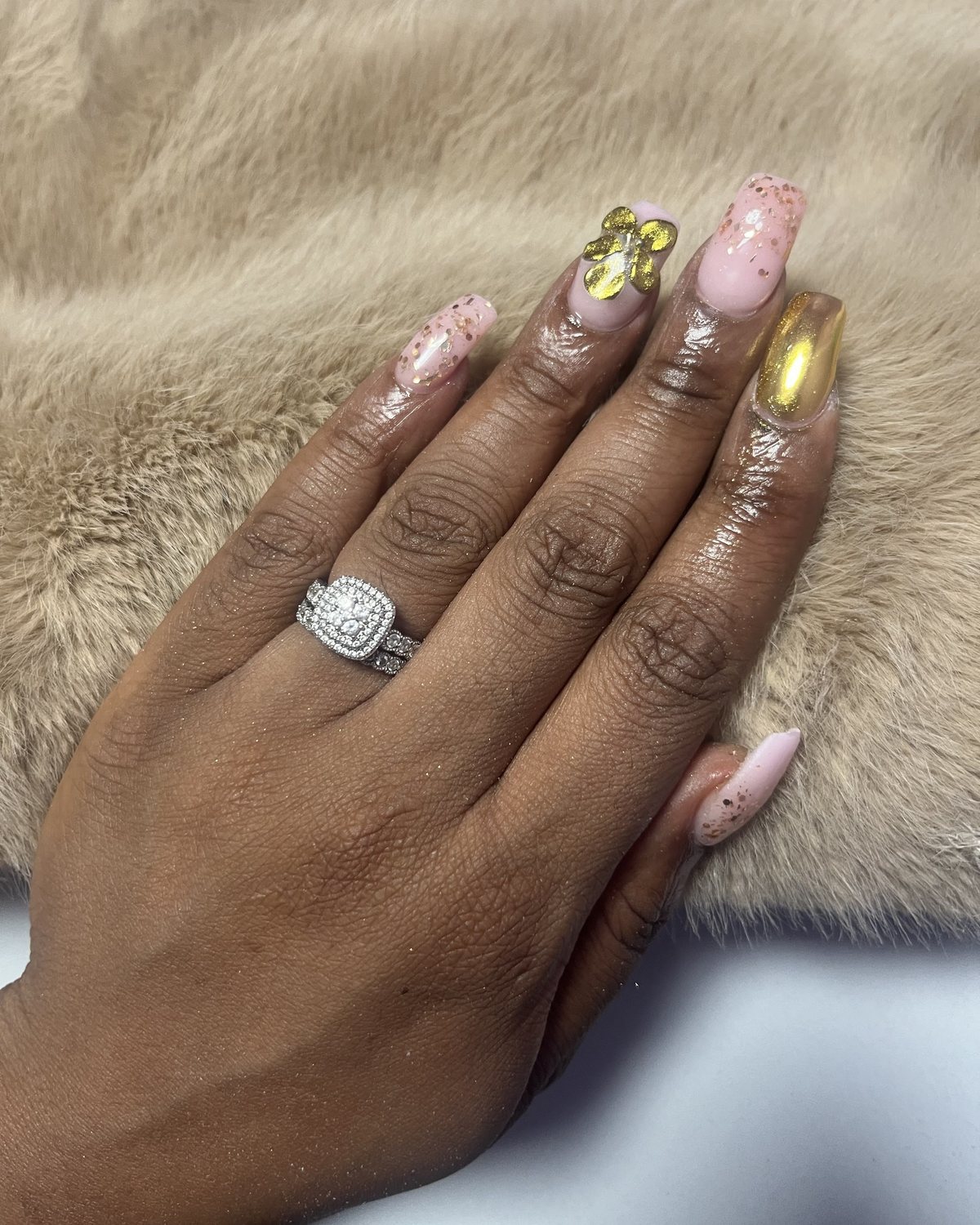Lichtroze nagels met goudvlokjes, een gouden 3D-strikje en een gouden chrome nagel